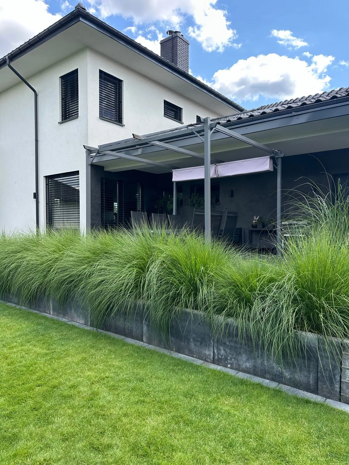 Pergola nad tarasem i trawy ozdobne w obrzeżu gabionowym